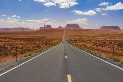 A straight two-lane highway running to the horizon across a flat desert