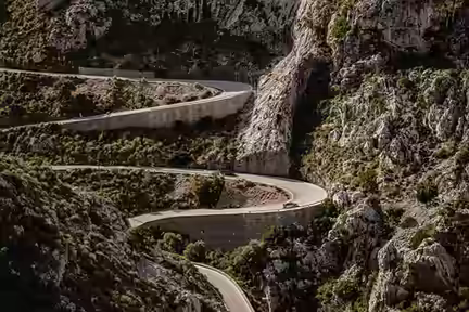 A narrow mountain road with tight hairpin bends on a rocky hillside